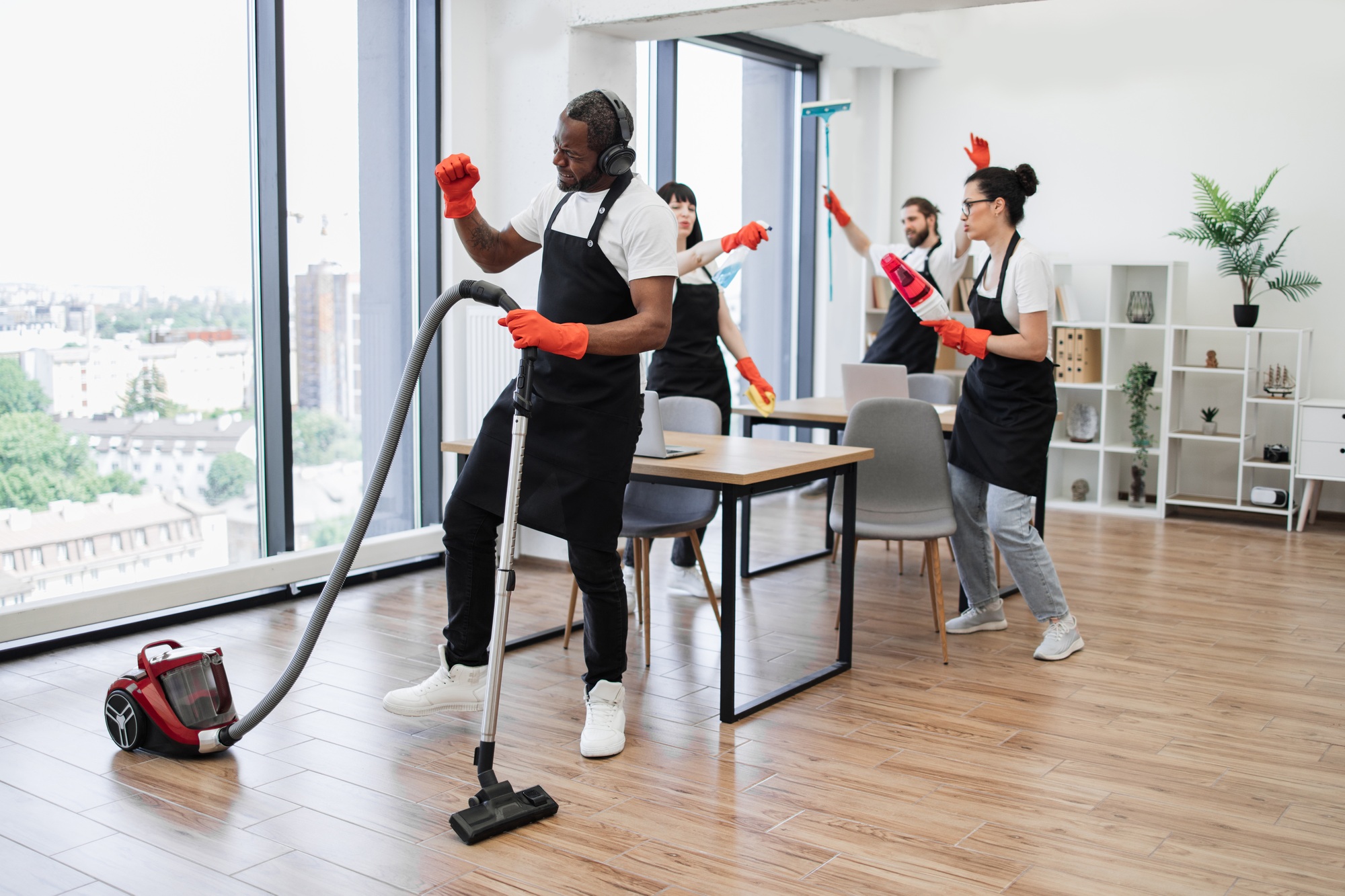 African man with modern vacuum cleaner and three cleaners dancing.